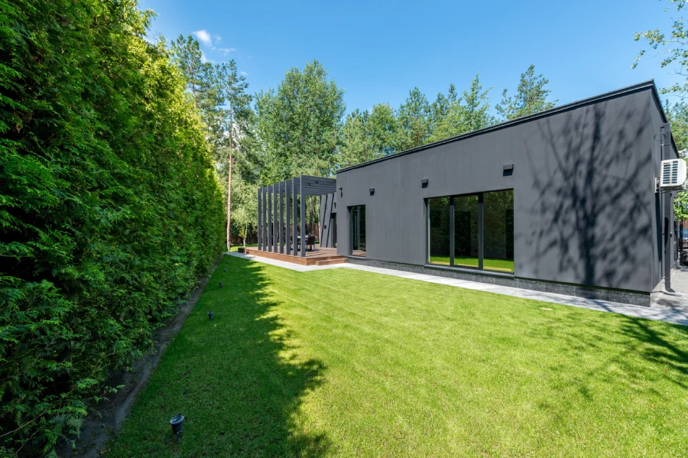 Neatly maintained lawn beside a modern home with tall hedges and outdoor entertaining area.